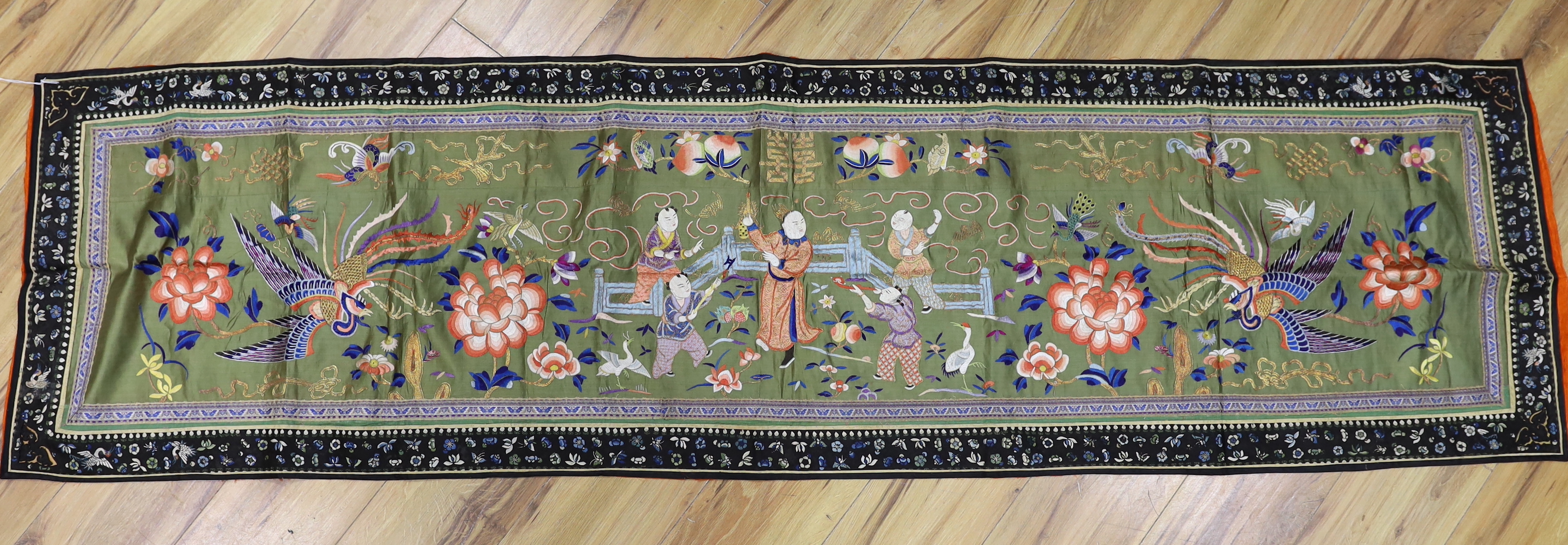 A long Chinese silk embroidered runner embroidered with the figure of Fu and boys, symbolic peaches, phoenix and flowers, possibly an altar cloth together with two other smaller runners, largest runner 202cm long x 55cm